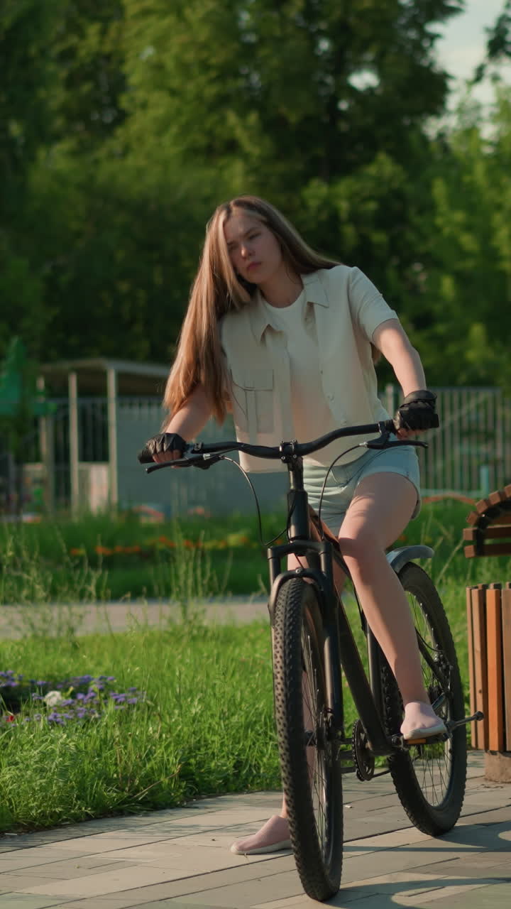 자전거 타는 사람은 활기찬 정원 근처에 자전거를 타고, 따뜻한 빛 아래 머리카락을 조정하고, 다채로운 꽃받침, 나무, 나무 벤치에 둘러싸여, 그녀는 야외 타기 위해 준비합니다.