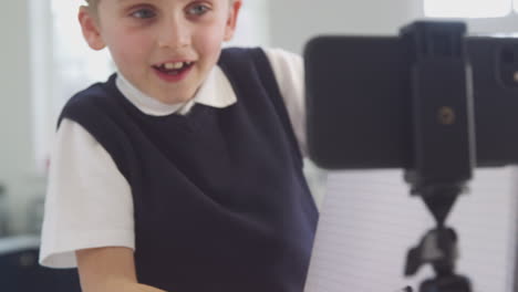 Niño-En-Casa-Usando-Uniforme-Escolar-Teniendo-Una-Lección-En-Línea-A-Través-De-Videollamada-En-Un-Teléfono-Móvil