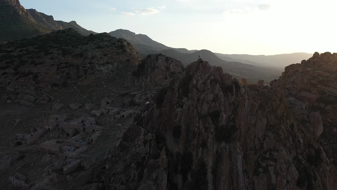 toma aérea avanzando, pasando la cima del pico donde una sola persona está sola, contemplando la épica y majestuosa vista y el paisaje después de una larga e intensa caminata