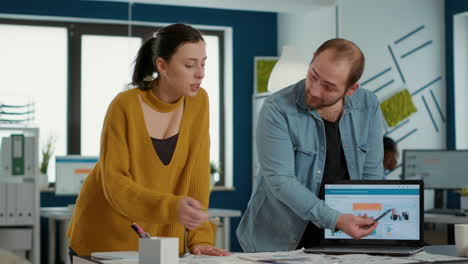 colegas en la oficina comparando papeles con gráficos de ventas con la evolución de la cuota de mercado en la pantalla del portátil