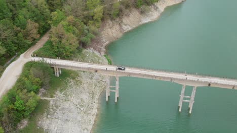 aerial drone view of the car crossing from a small bridge over turano lake, lazio, italy