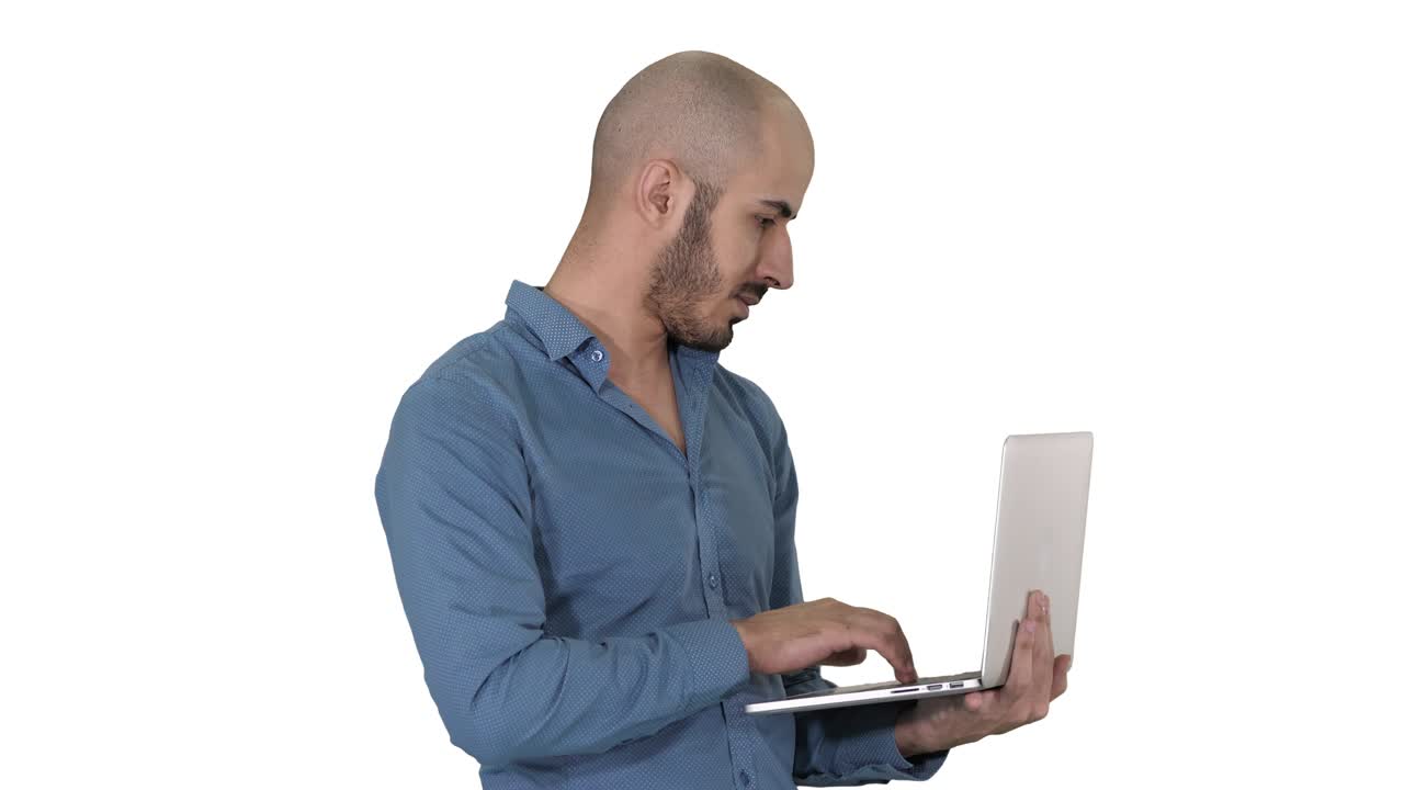 joven empresario de oriente medio, de pie y escribiendo en una computadora portátil cuando la sostiene en sus manos sobre un fondo blanco