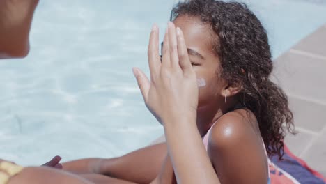 madre y hija afrodescendientes felices aplicando protector solar junto a la piscina, cámara lenta