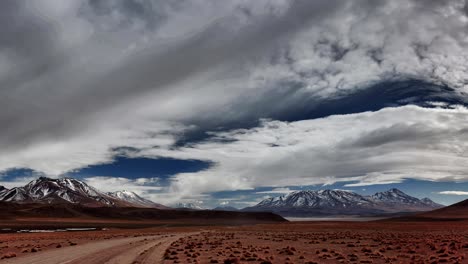 amplia escena panorámica del paisaje andino boliviano y camino de tierra con cielo nublado y montañas cubiertas de nieve en el fondo, bolivia