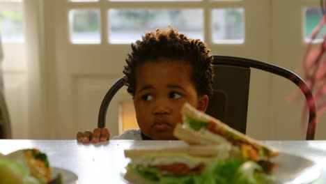 front view of cute little black boy sitting on chair at dining table in a comfortable home 4k