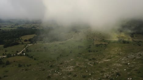 vista aérea del parque nacional de velebit: volando a través de las nubes parque con carretera de grava y árboles en croacia