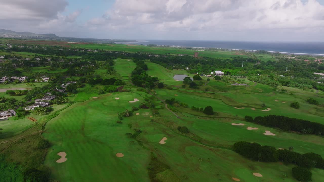 Golf hotel coast Indian ocean. Golf course and villas on the beach. Aerial view of Golf course. Establishing shot, drone flying over golf club. Summertime, sunset. The life of rich people. Mauritius