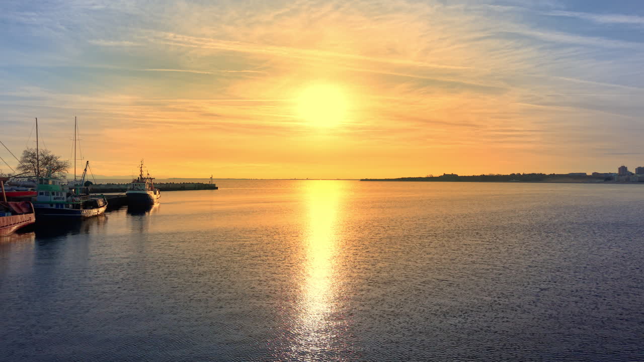 Fishing boats at sunset with sun path reflecting on the sea surface. Sun reflection on water in a peaceful harbor. Aerial view