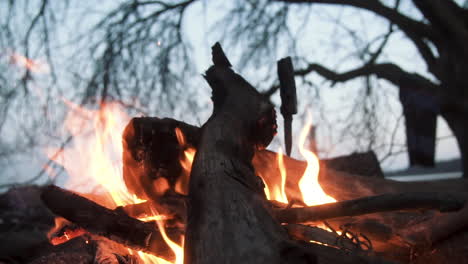 Man-stabs-knife-in-wood-lock-at-Bonfire-sparks-outdoor-wilderness-close-up-slow-motion