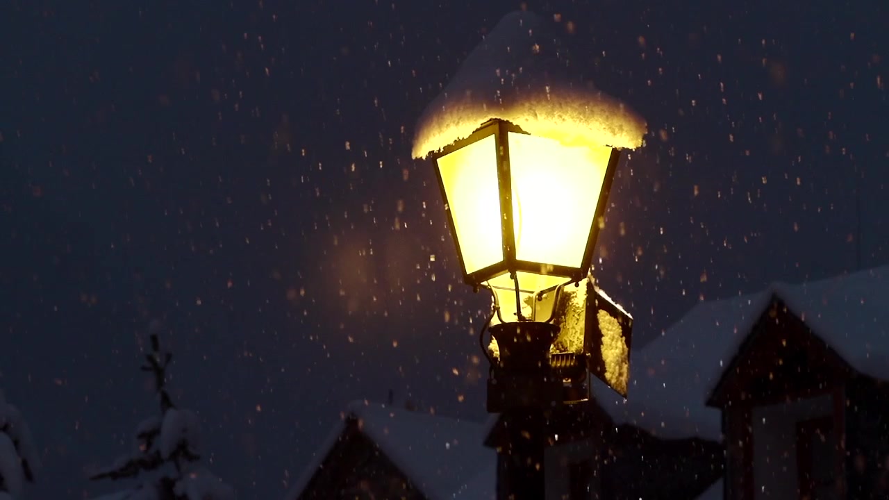 Ripresa al rallentatore di un lampione che illumina la neve durante una nevicata notturna. La ripresa inizia sfocata e mette a fuoco dolcemente