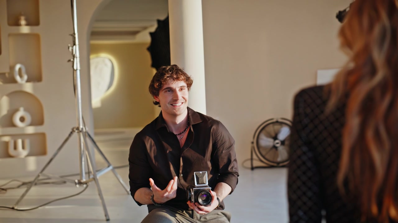 Man holding vintage camera talking model photo studio. Photographer gesturing.