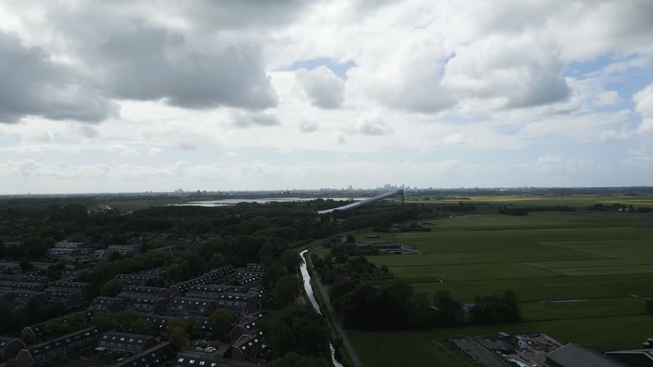 Unique drone shot of an artificial snow slope structure extending across lush green fields with a distant city skyline.