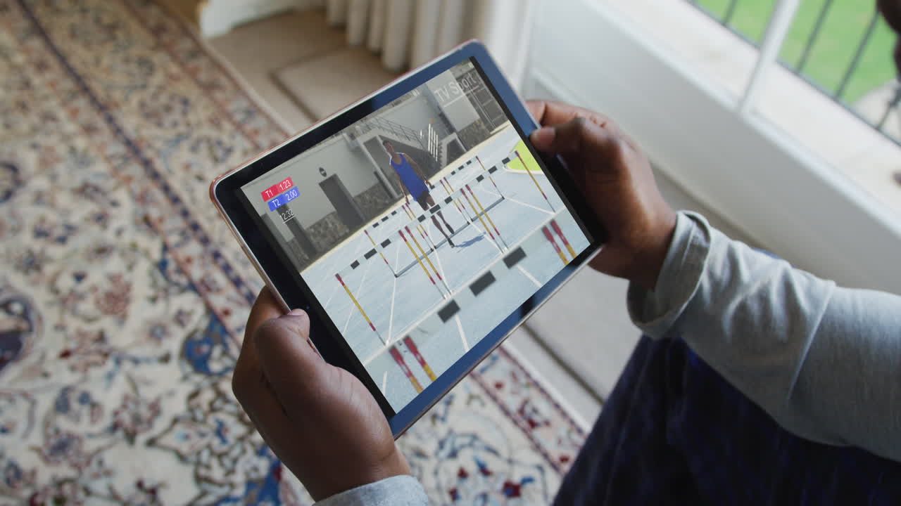 Composite of man sitting at home, watching athletics running event on tablet