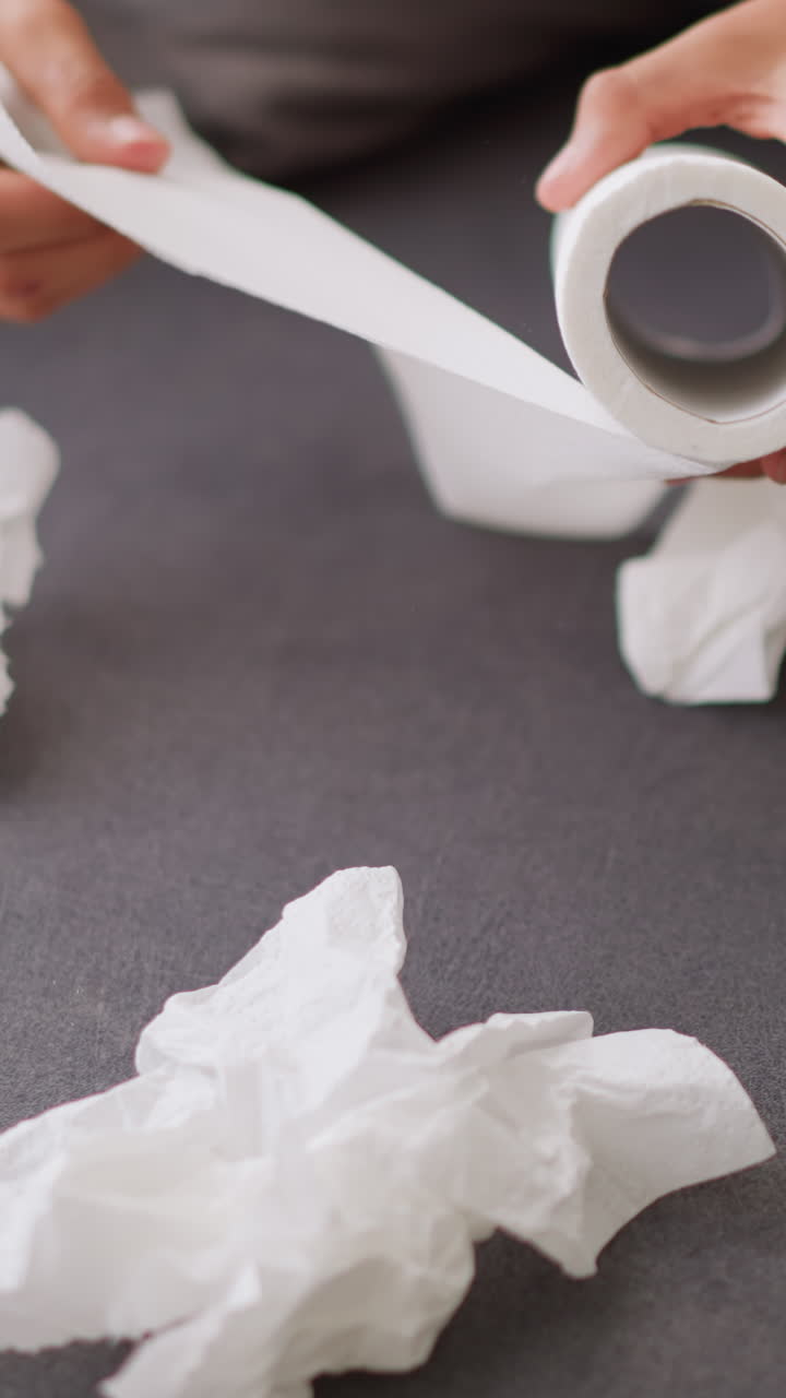 Close-up of hand reaching for tissue roll as used tissues lie on couch, sick person recovering at home, using tissues, with clutter around, and comfort of being at home
