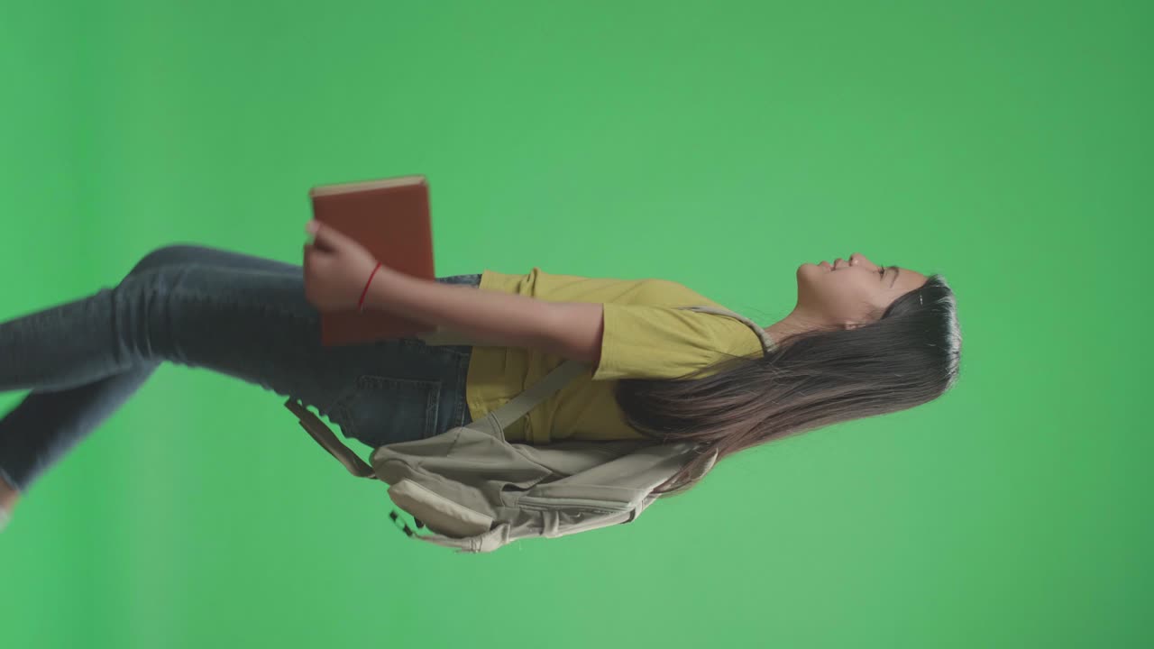 vista lateral de una estudiante asiática sosteniendo un libro mientras camina a la escuela en pantalla verde clave de croma