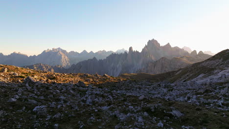 Flying-across-rugged-sunlit-Tre-Cime-vast-rocky-alien-landscape-aerial-view-towards-majestic-dolomites