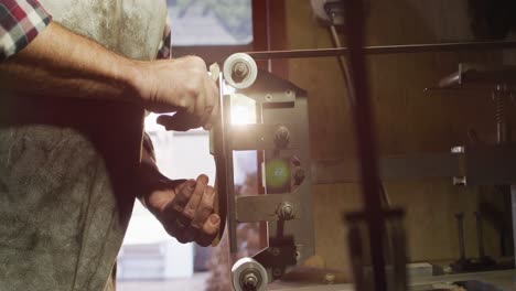 close up of caucasian male knife maker in workshop holding knife and using sander