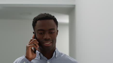 close up of smiling young businessman walking along corridor in office talking on mobile phone 1