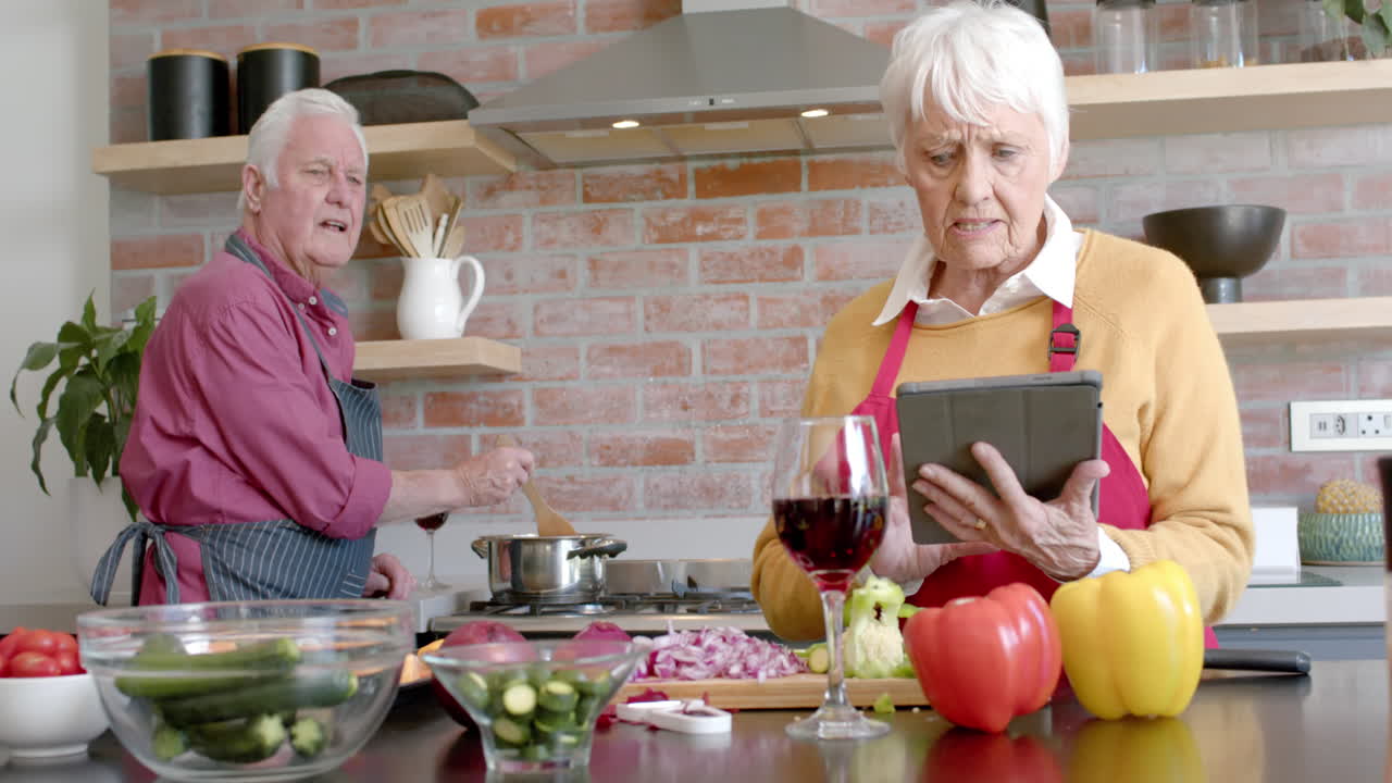 una pareja caucásica senior cocinando la cena usando una tableta en la cocina en casa, en cámara lenta.