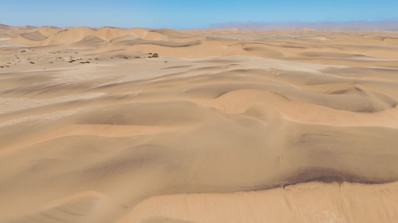 High-altitude aerial shot of the Namib Desert coastline near Swakopmund, showing endless dunes fading into the Atlantic horizon
