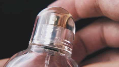 persona pone la tapa de la botella de perfume de las mujeres en un fondo oscuro