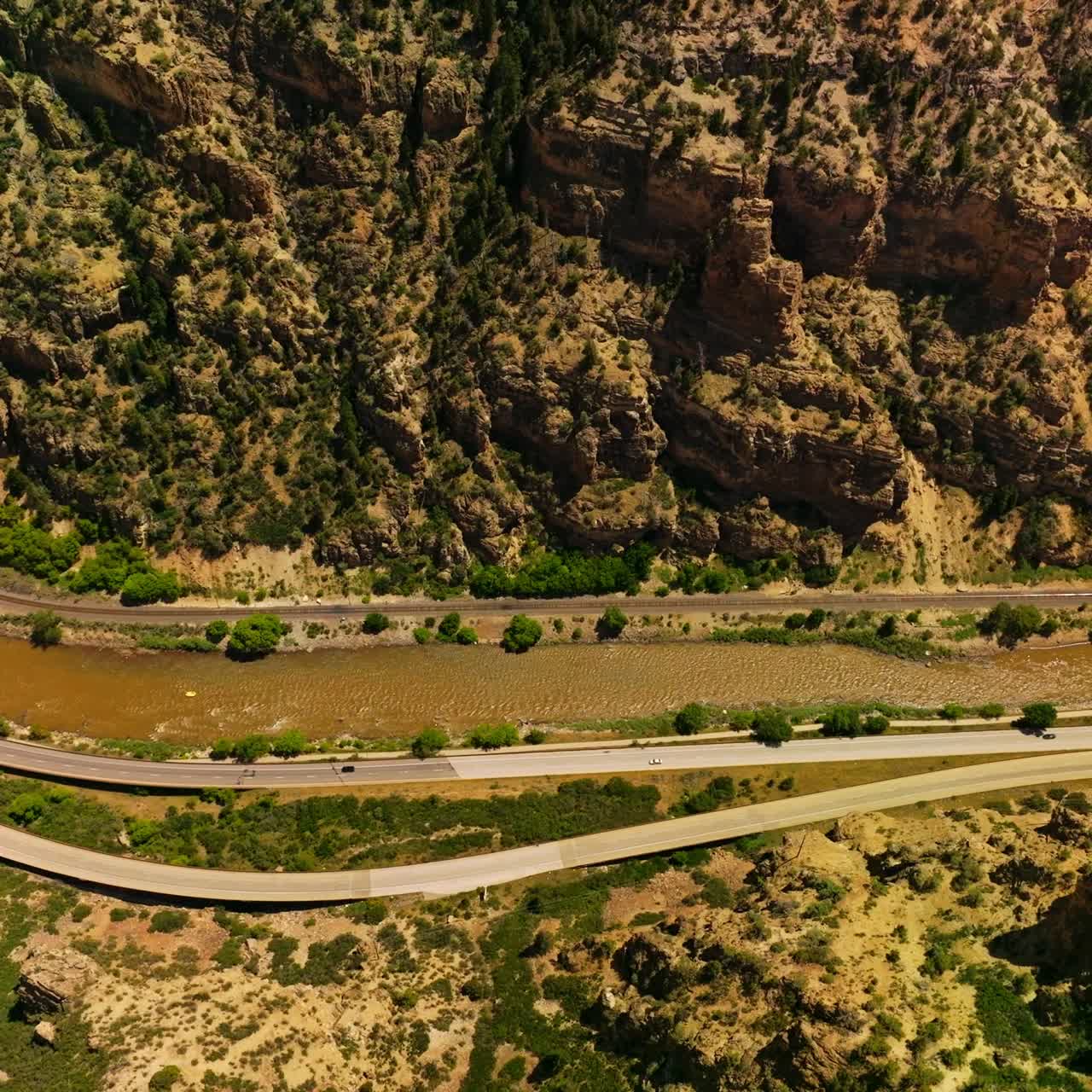 Narrow river flowing at the foot of a mountain. Two highways going by the waterfront of the river in Colorado, USA. Aerial view