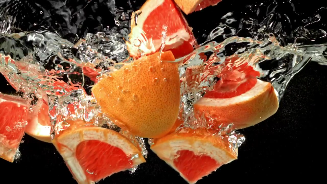 Frische Grapefruitscheiben fallen und spritzen ins klare Wasser