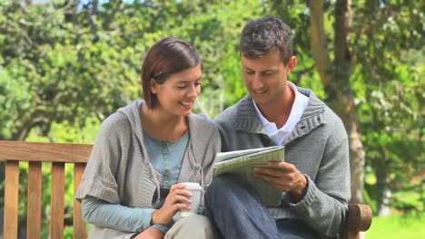 young couple doing crosswords on a bench