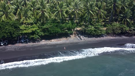 secret oasis: aerial 4k orbiting drone view of a lone girl lying on the untouched black sand beach in gretek, bali