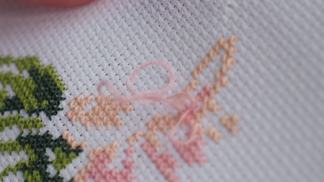 Extreme close up of skilled person embroidering colorful pattern on white fabric, delicate needlework forming tree like design with green and peach threads