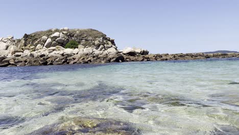 Schwenkaufnahmen-Einer-Von-Klarem-Wasser-Umgebenen-Insel,-Sichtbarer-Meeresboden-Mit-Algen