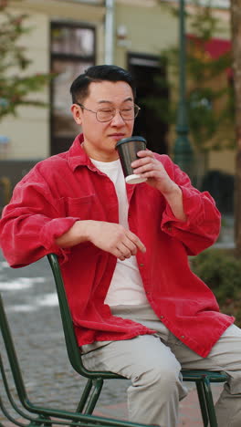 happy asian man enjoying drinking morning coffee hot drink, relaxing, taking a break on city street