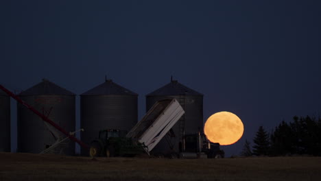 Timelapse-De-Teleobjetivo-De-Luna-Llena-Saliendo-Detrás-De-Silos-De-Grano-Durante-La-Cosecha