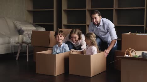 una pareja juguetona empuja a hermanos alegres sentados dentro de cajas de cartón.