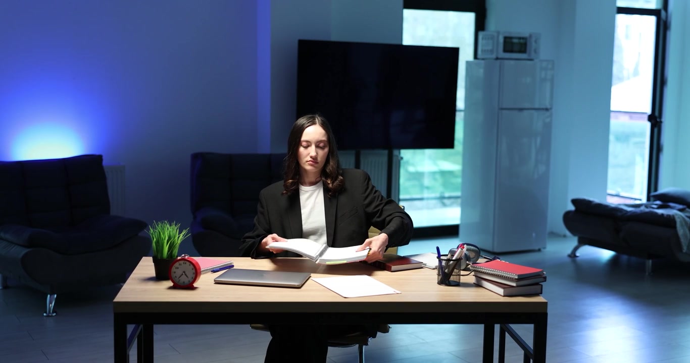Donna in giacca formale siede a una scrivania di legno esaminando documenti.
