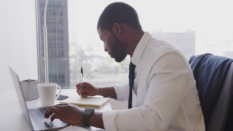 Hombre-De-Negocios-Trabajando-En-El-Escritorio-Con-Una-Computadora-Portátil-En-Una-Oficina-Moderna-Revisando-Datos-En-Un-Reloj-Inteligente