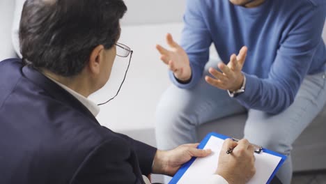 male psychologist listening to man with psychological problems and making notes on paper.