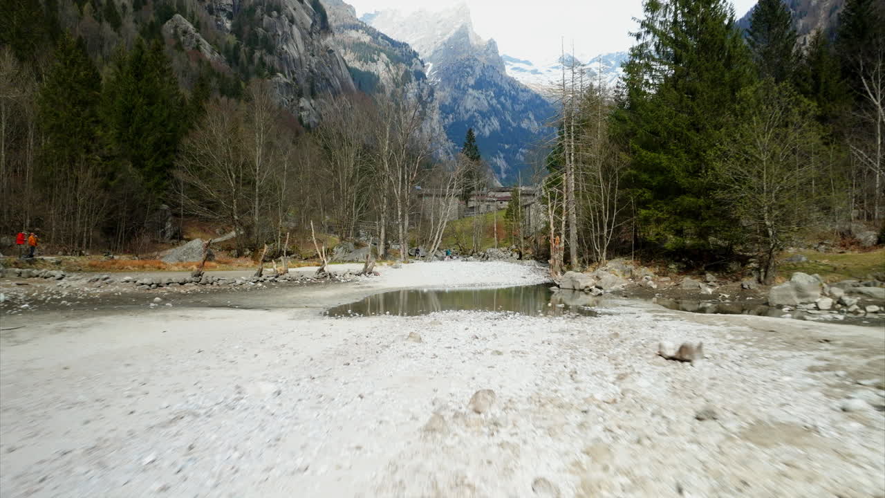 Ground-level aerial view of hiking trail in valley of Val di Mello Natural Reserve, Italy with idyllic woodlands and shallow river