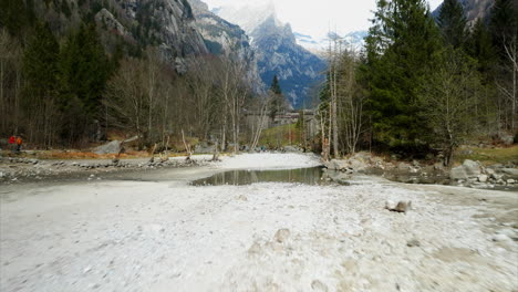 Ground-level-aerial-view-of-hiking-trail-in-valley-of-Val-di-Mello-Natural-Reserve,-Italy-with-idyllic-woodlands-and-shallow-river