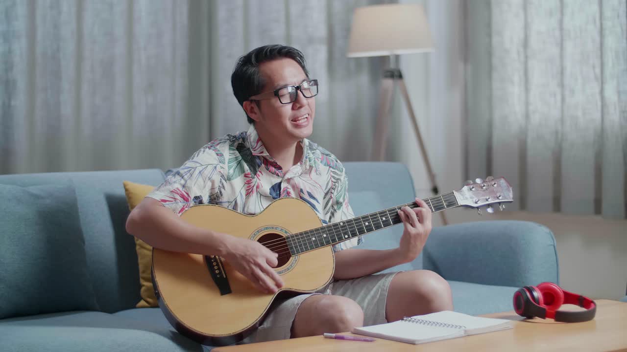 테이블 위에 노트북을 들고 집에서 노래하고 기타를 연주하는 아시아인 작곡가
