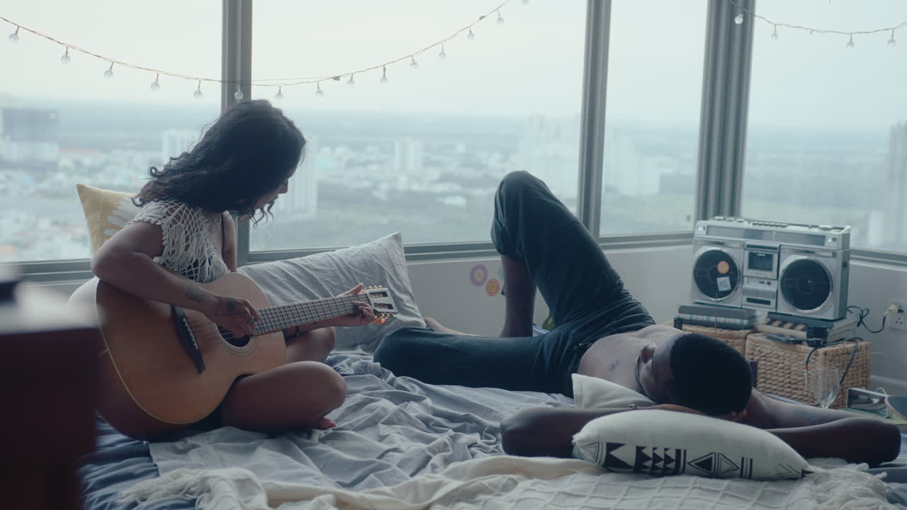 Young Woman Playing the Guitar and Singing for Her Boyfriend at Home