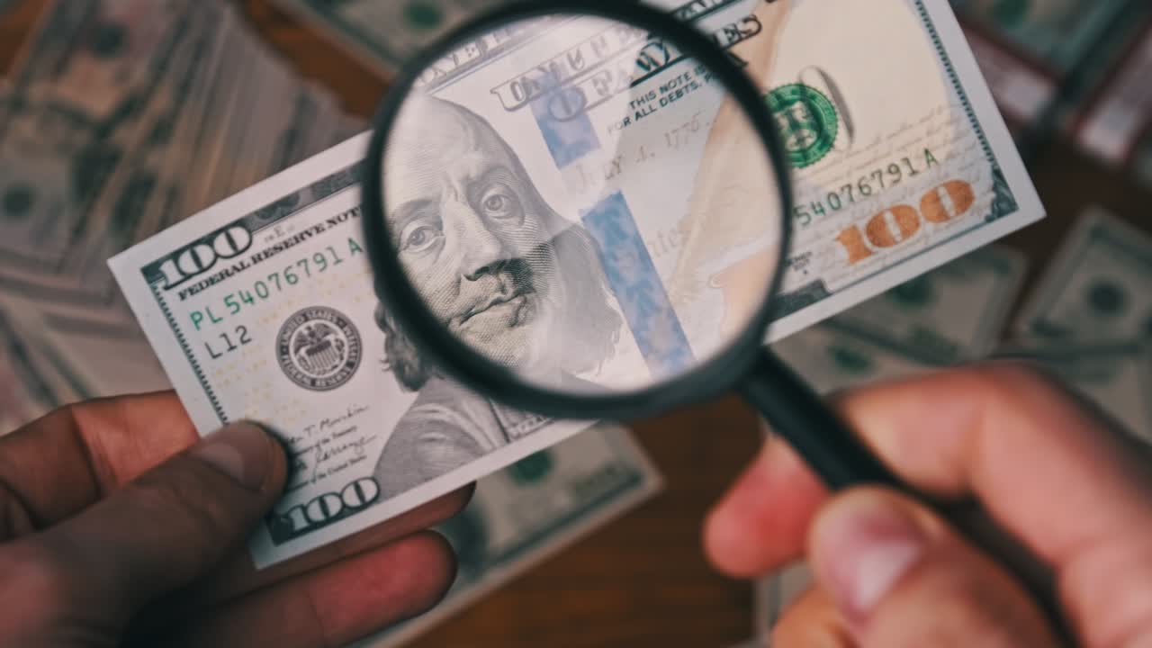 cento dollari ispezionando sotto una lente d'ingrandimento sullo sfondo del denaro