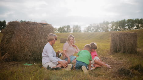 familia feliz reunida en una manta a cuadros en el campo abierto, disfrutando de un picnic al aire libre con bocadillos, la luz del sol proyecta un brillo cálido, con balas de heno y árboles en el fondo