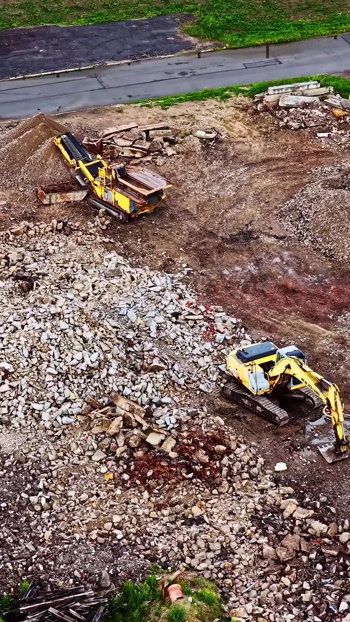 Industrielt udstyr, herunder en kæbeknuser og gravemaskine, der bearbejder sten og murbrokker på en byggeplads.