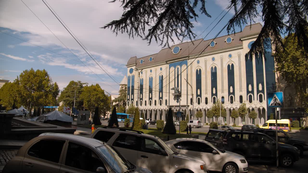 Tbilisi, Georgia parliament building with waving flags, clouds and blue sky.