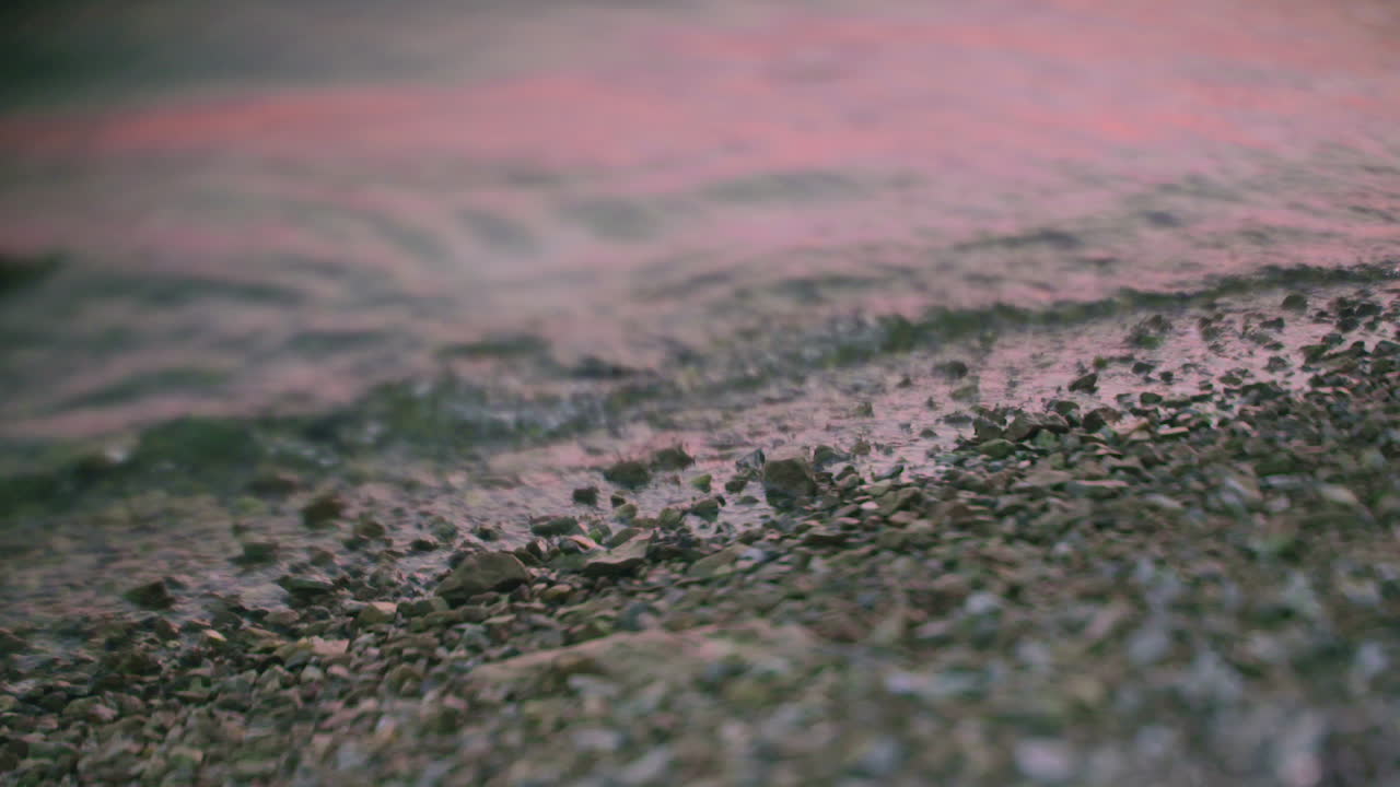 Gentle Waves Washing Over Pebbles with Pink Sunset Reflection