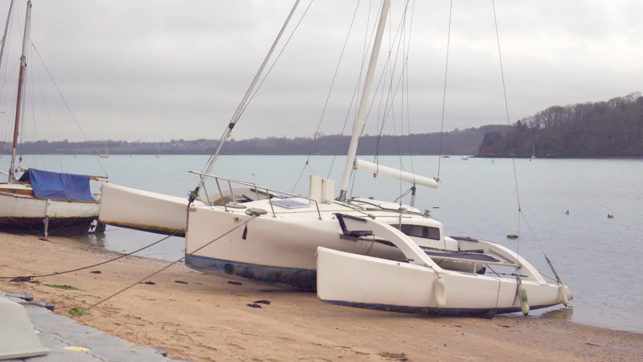 A catamaran sits quietly between the sand and the sea on a small Breton beach during low tide. The calm winter atmosphere creates a peaceful maritime scene.