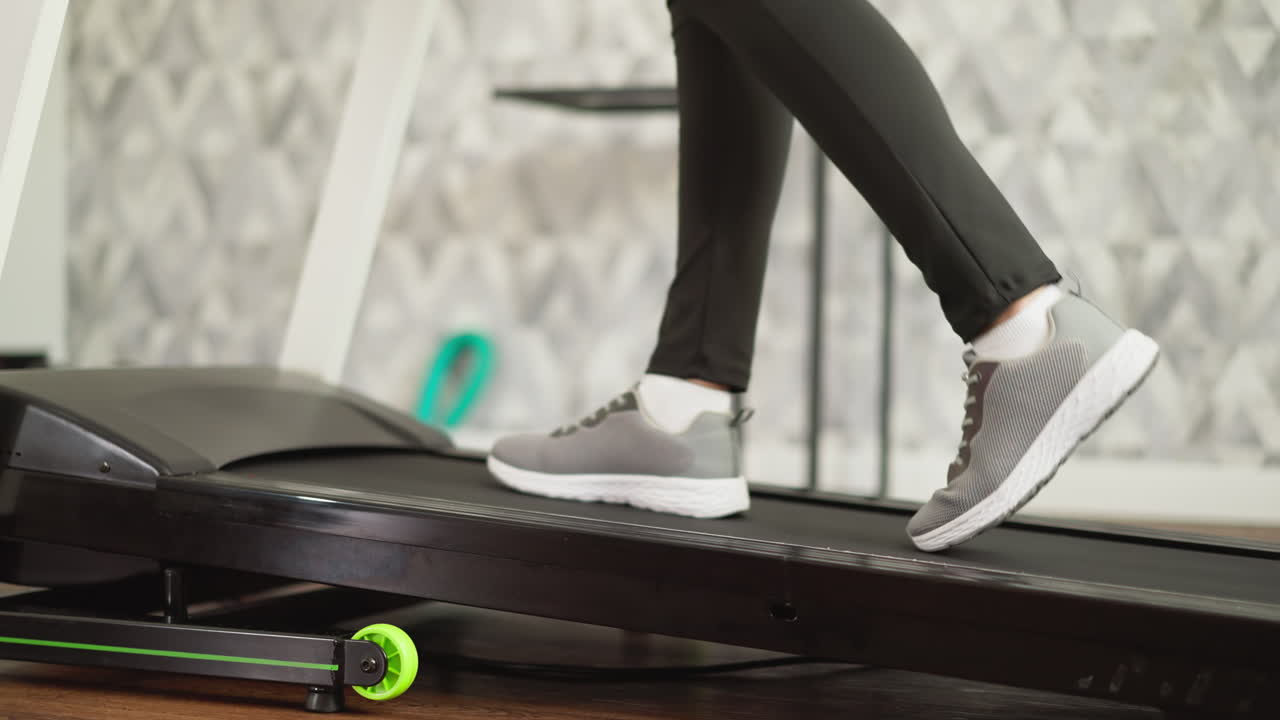 Woman strides on treadmill at residence closeup. Sporty woman maintains health by doing legs exercises on automated apparatus in private gym