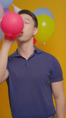 retrato vertical de estudio de video de un hombre con un sombrero de fiesta celebrando su cumpleaños soplando un globo