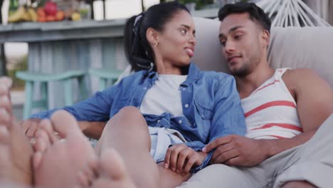 Happy-diverse-couple-relaxing-in-hammock-together-and-talking-at-beach-bar,-in-slow-motion